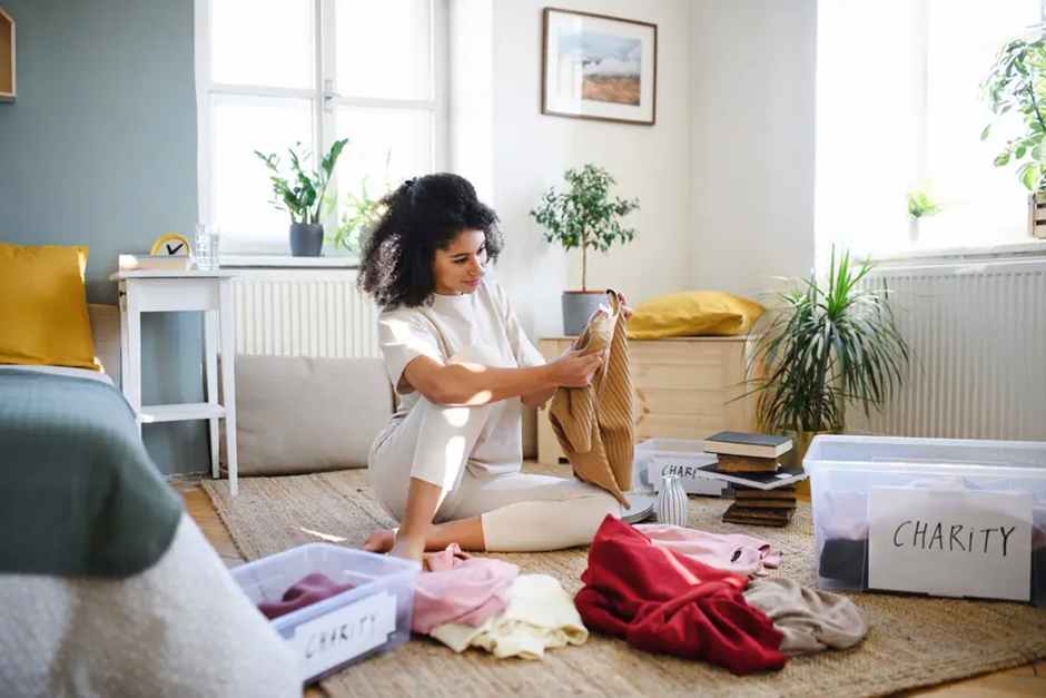 Woman organizing clothes for charity donation in a bright bedroom