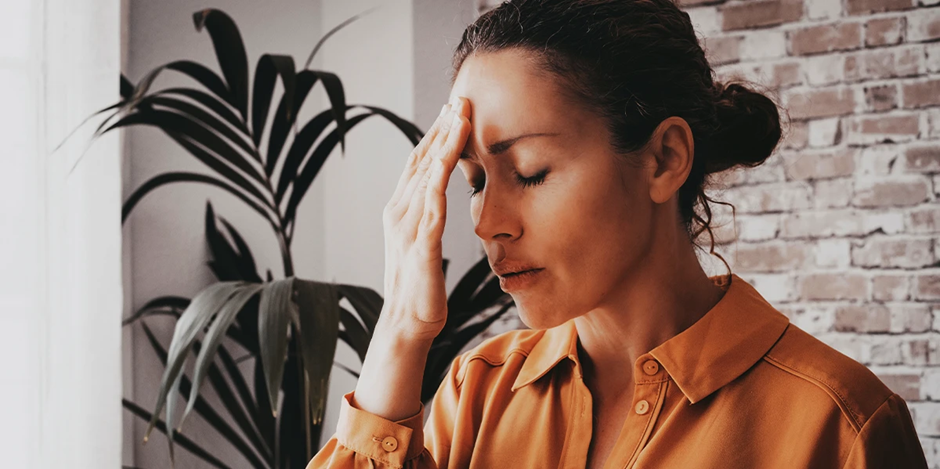 Woman experiencing stress and headache indoors, touching forehead in discomfort.