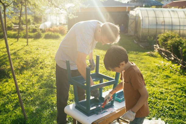 A father and son painting a stool outside.