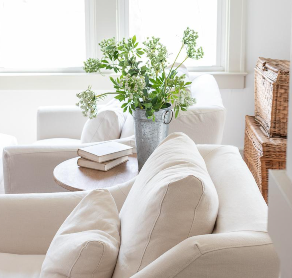 Bright living room with white sofa, wooden side table, and fresh flowers in a metal vase
