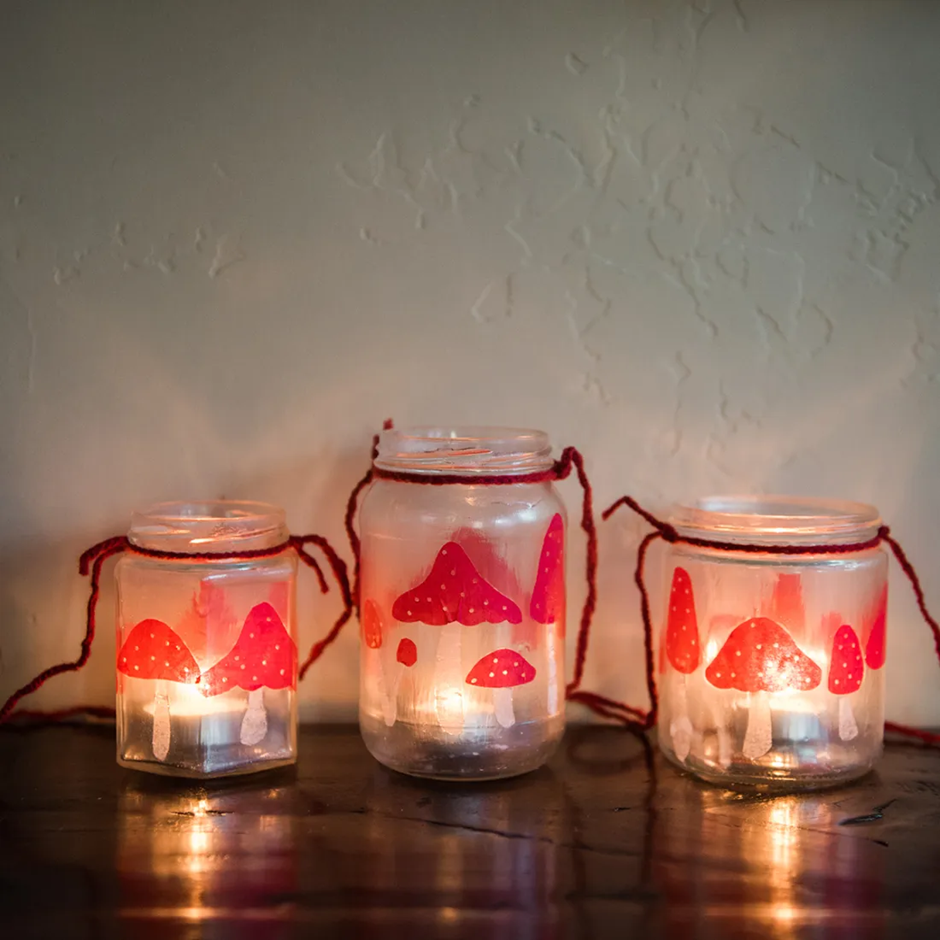 DIY mason jar lanterns with red mushroom designs glowing with candles inside