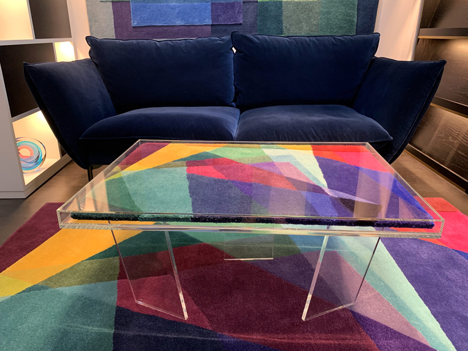 Modern living room with a navy blue sofa, clear acrylic coffee table, and a colorful geometric rug