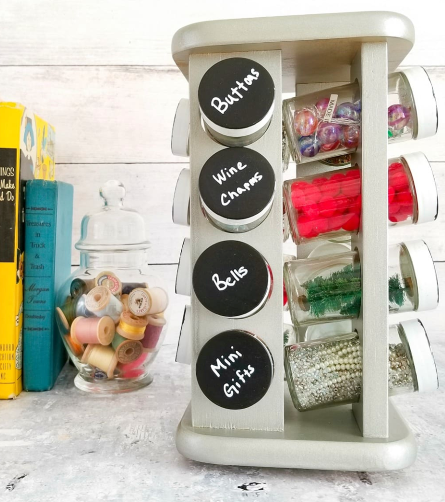 Rotating spice rack repurposed as a craft storage organizer holding mini jars of buttons, bells, pom-poms, and beads