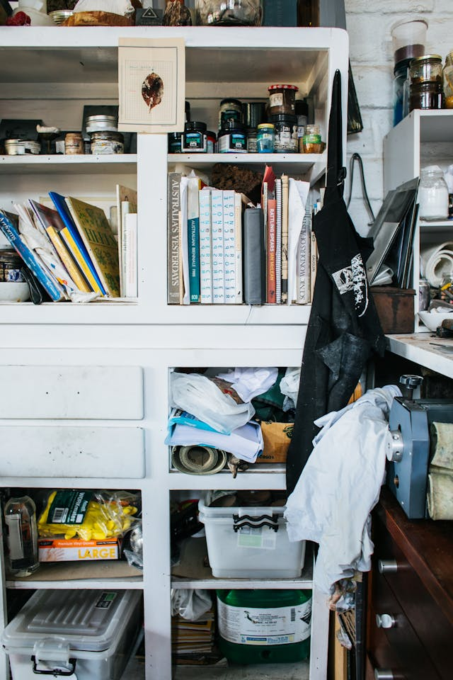 A shelf cluttered with books and containers scattered everywhere.