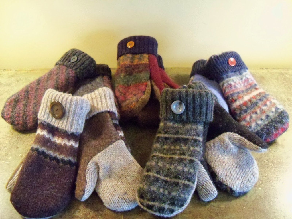 A collection of handmade mittens sewn from recycled wool sweaters, featuring various colors, patterns, and buttoned cuffs.
