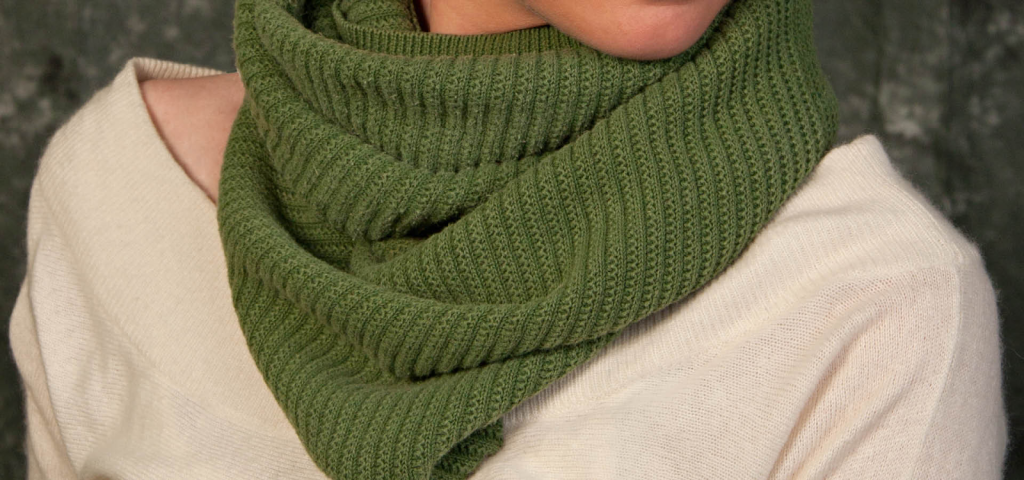 A close-up of a soft green knit scarf wrapped around a person’s neck, made from repurposed sweater fabric.