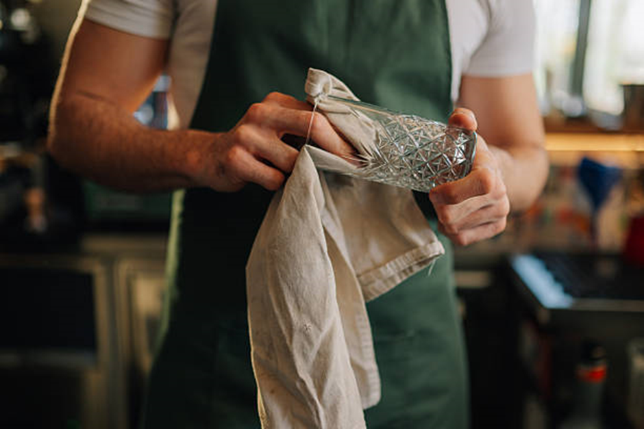 person drying a patterned glass cup with a cloth in the kitchen