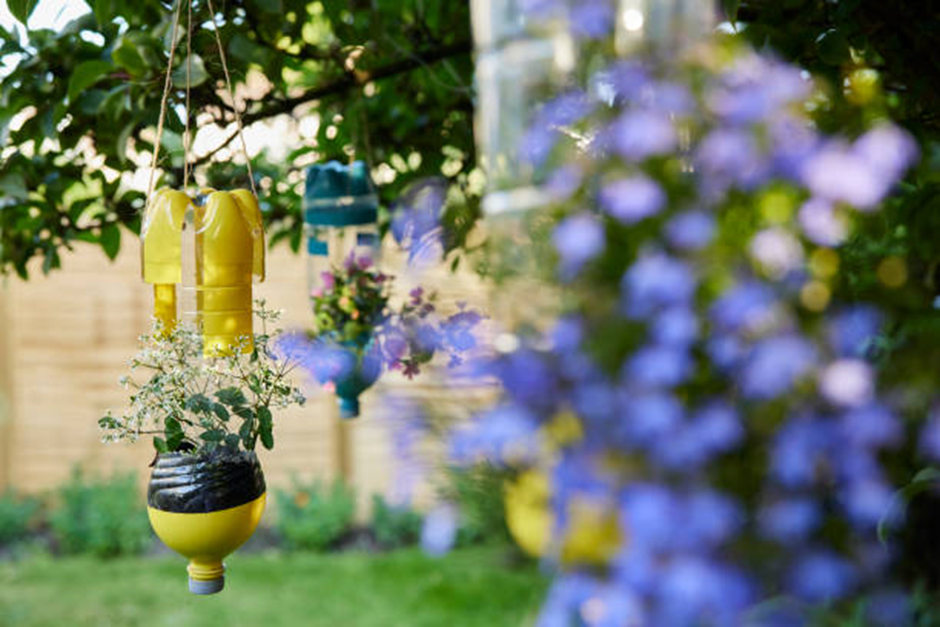 upcycled hanging plastic bottle planters filled with flowers in a garden