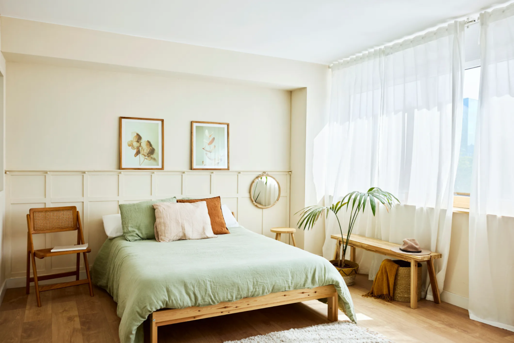 Bright minimalist bedroom with soft green bedding, natural wood furniture, and large sheer curtains