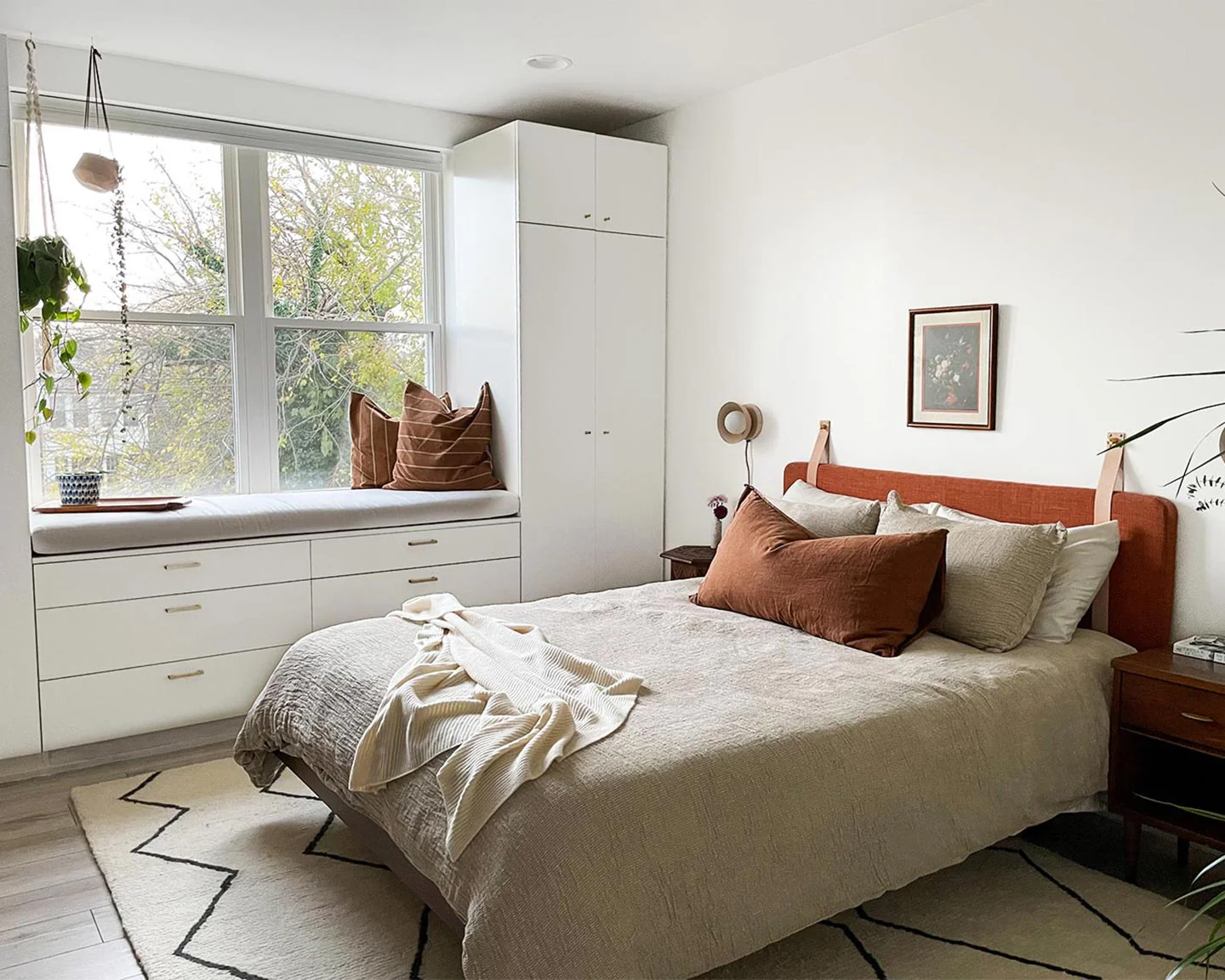 Modern cozy bedroom with built-in window seat, white storage cabinets, and warm brown pillows on a neutral bed