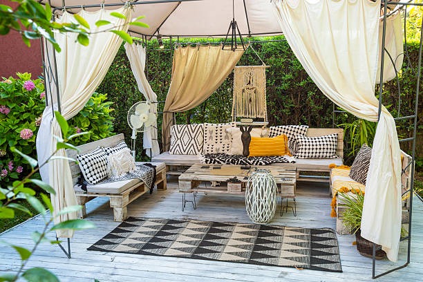 Bohemian-style outdoor lounge with draped curtains, patterned cushions, and wooden furniture