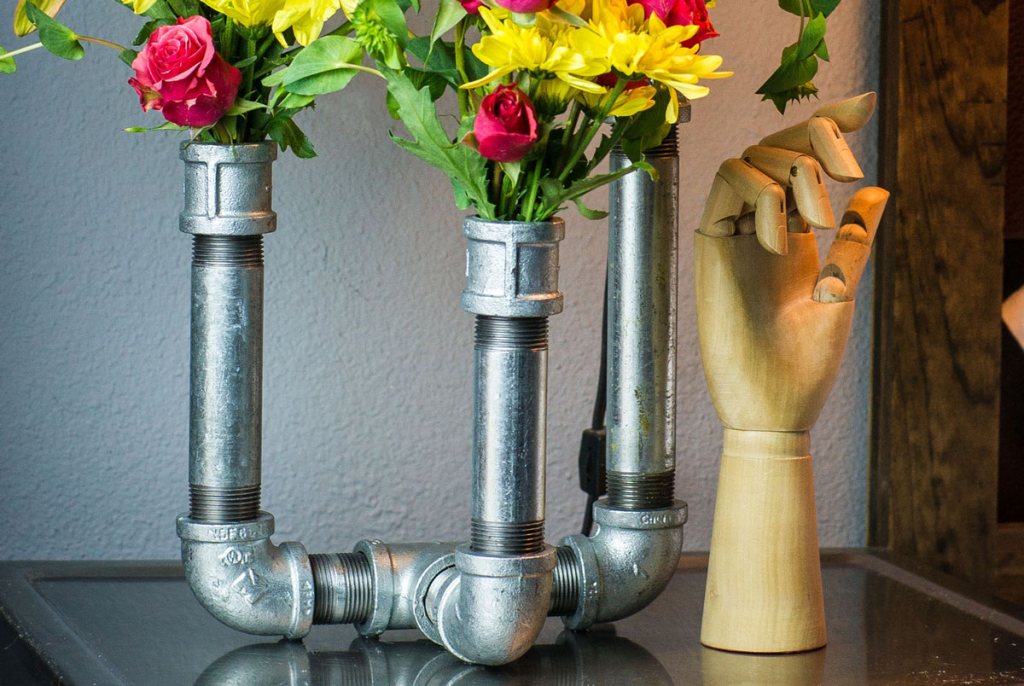 Industrial pipe vase holder with metal pipes supporting colorful fresh flowers.