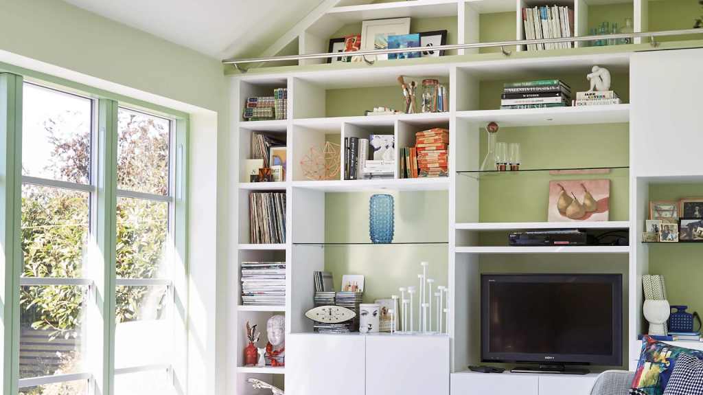 A built in shelving entertainment system on a light green wall in a living room.