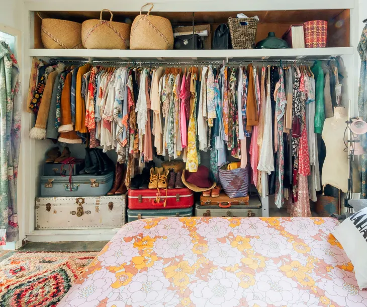 colorful organized closet with suitcases on the floor.