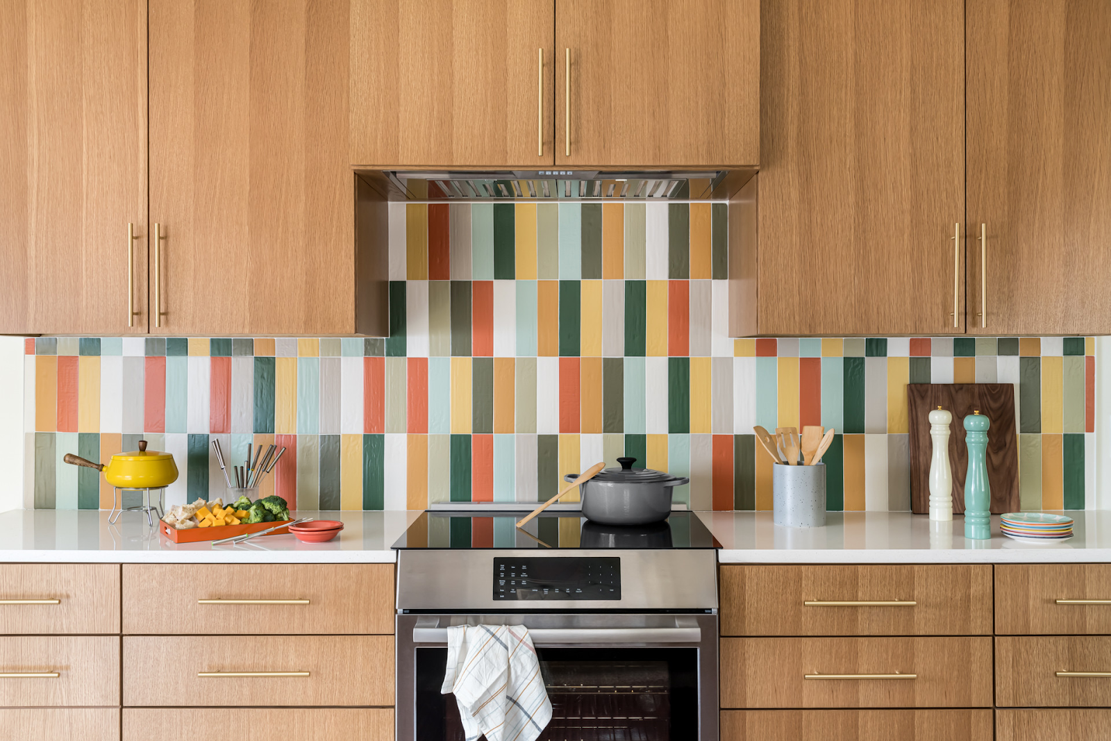 Modern kitchen with colorful vertical tile backsplash, wooden cabinets, and built-in stainless steel oven