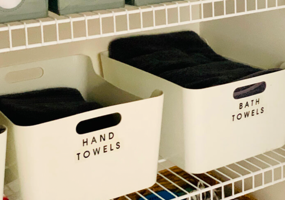 Labeled closet bins for hand towels and bath towels arranged on wire shelving for linen organization