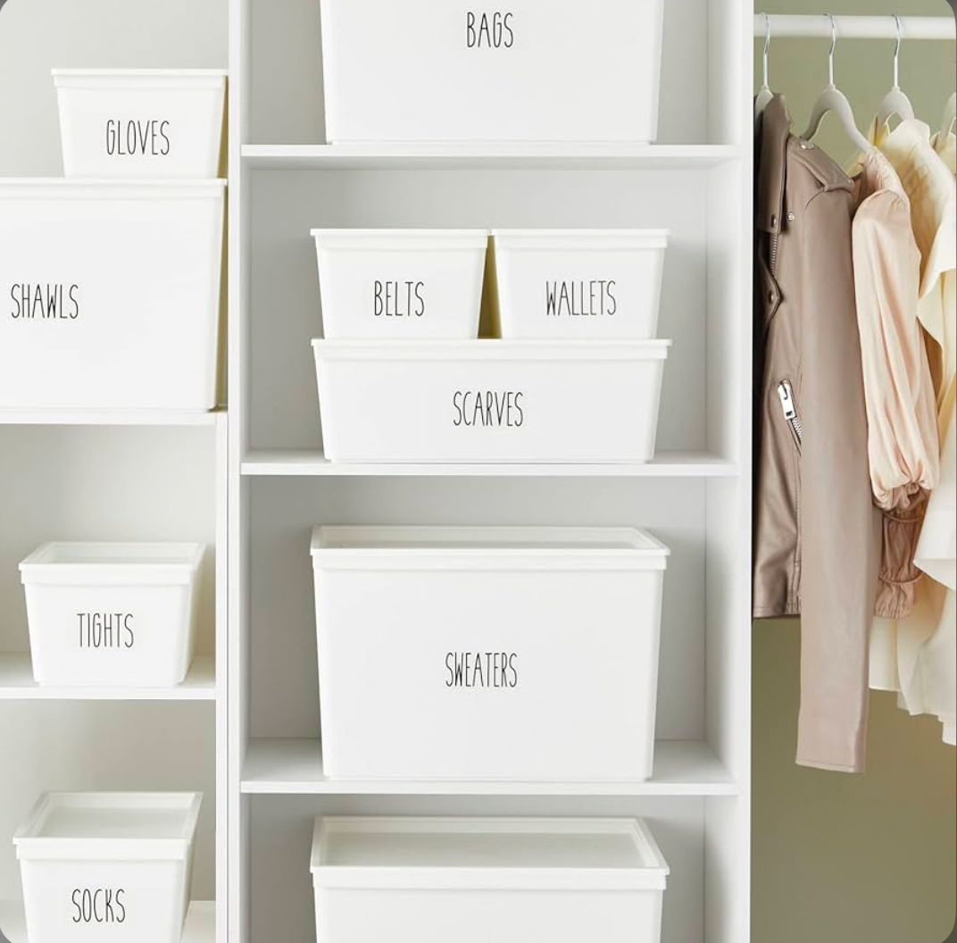 Labeled white storage bins organizing gloves, scarves, belts, wallets, and sweaters inside a minimalist closet shelving system