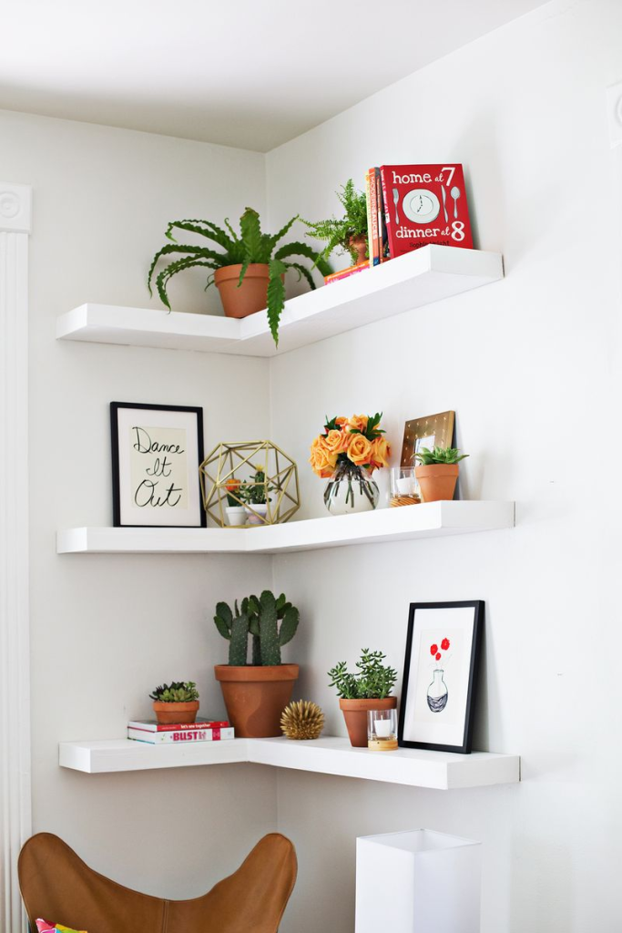 Modern white corner floating shelves decorated with plants, books, and framed wall art