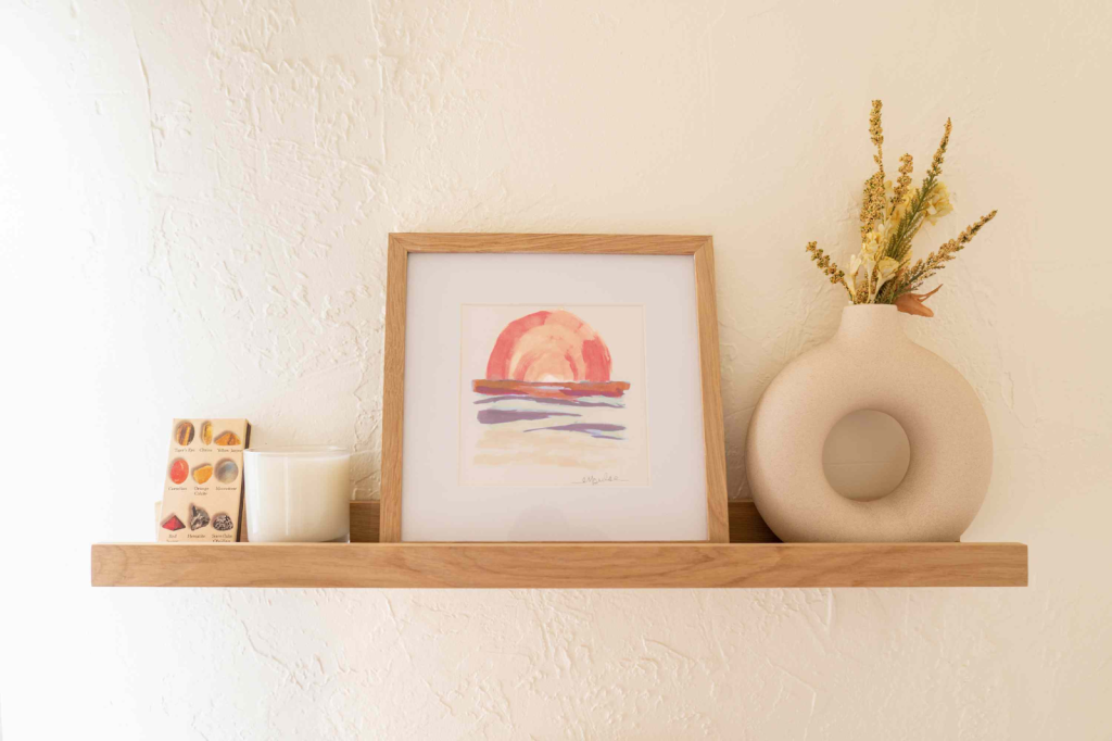 Minimal wooden floating shelf with framed artwork, candle, and ceramic vase decor