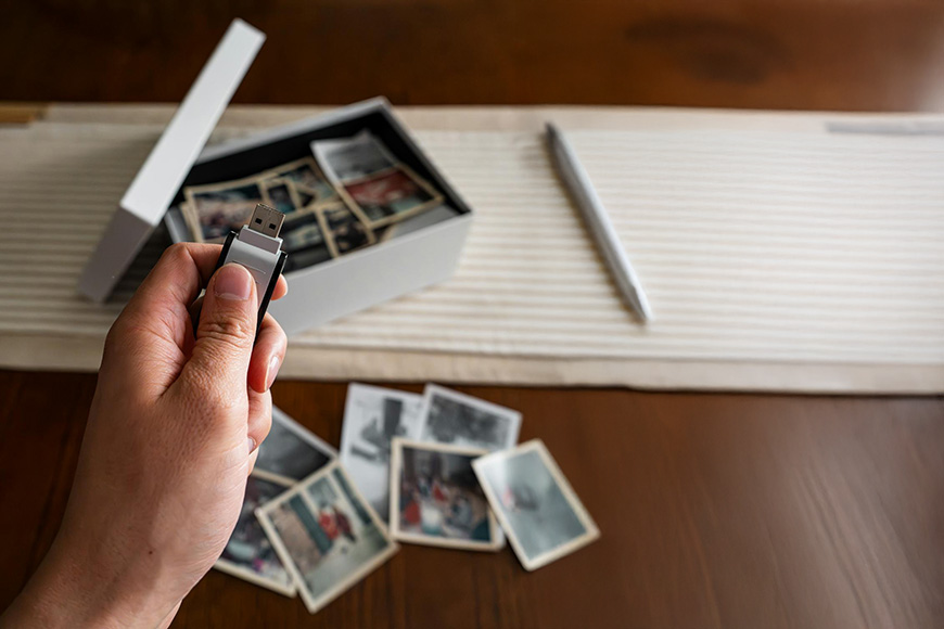 Hand holding USB flash drive with printed photos and storage box on wooden table