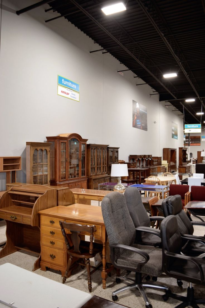 Secondhand furniture store aisle with wooden desks, cabinets, and office chairs on display.