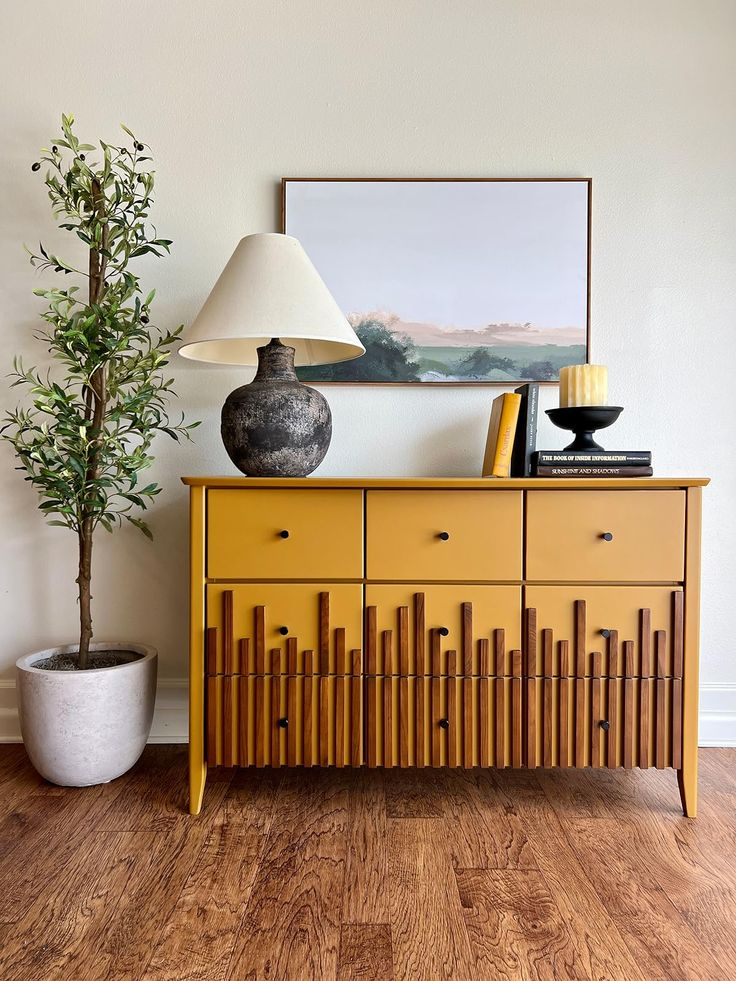 Mustard yellow mid-century modern sideboard with decorative wall art and indoor plant.