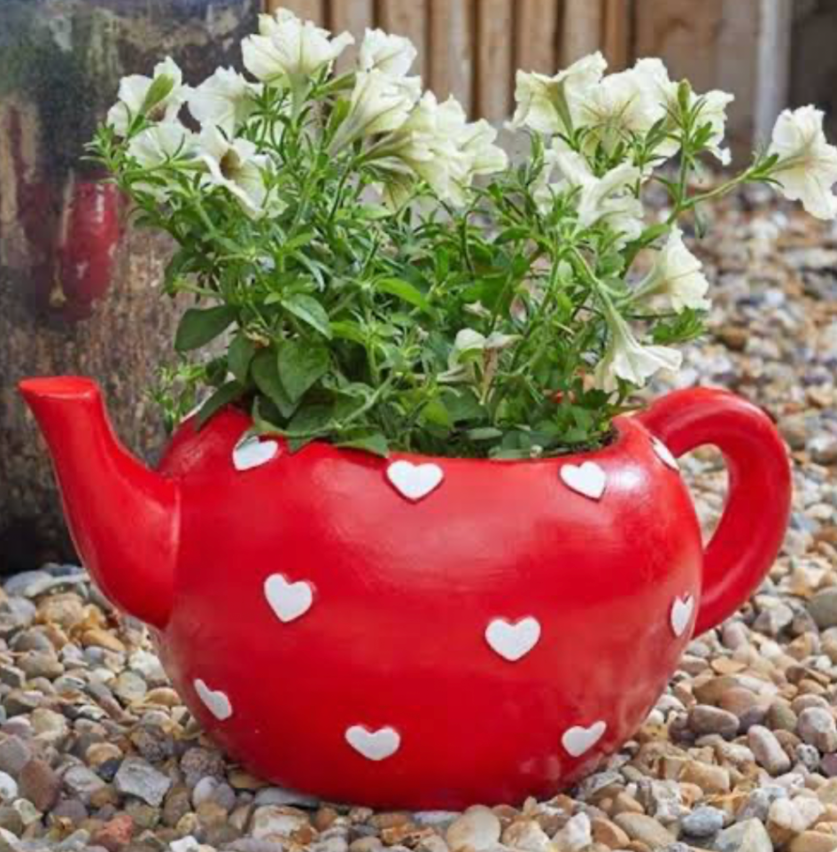 Red teapot planter with white heart design used as a decorative flower pot in garden landscaping