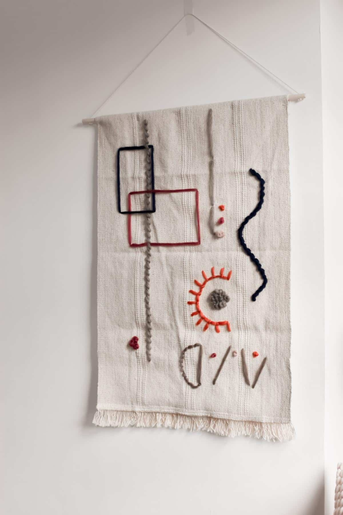 Handwoven textile wall hanging with abstract embroidery patterns and neutral boho decor style