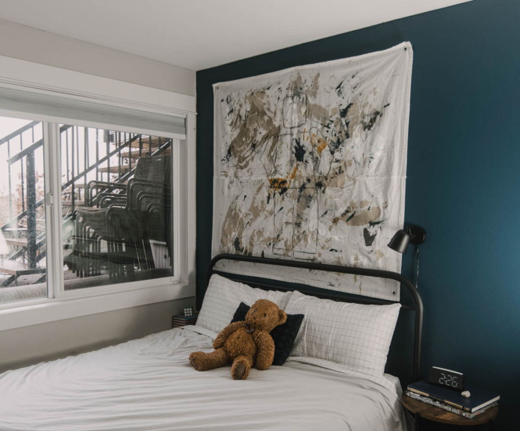 Abstract fabric wall tapestry hanging above bed in modern bedroom with dark accent wall