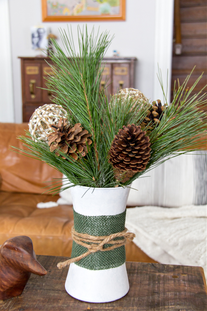 DIY winter centerpiece with pine branches, pinecones, and decorative balls in white vase