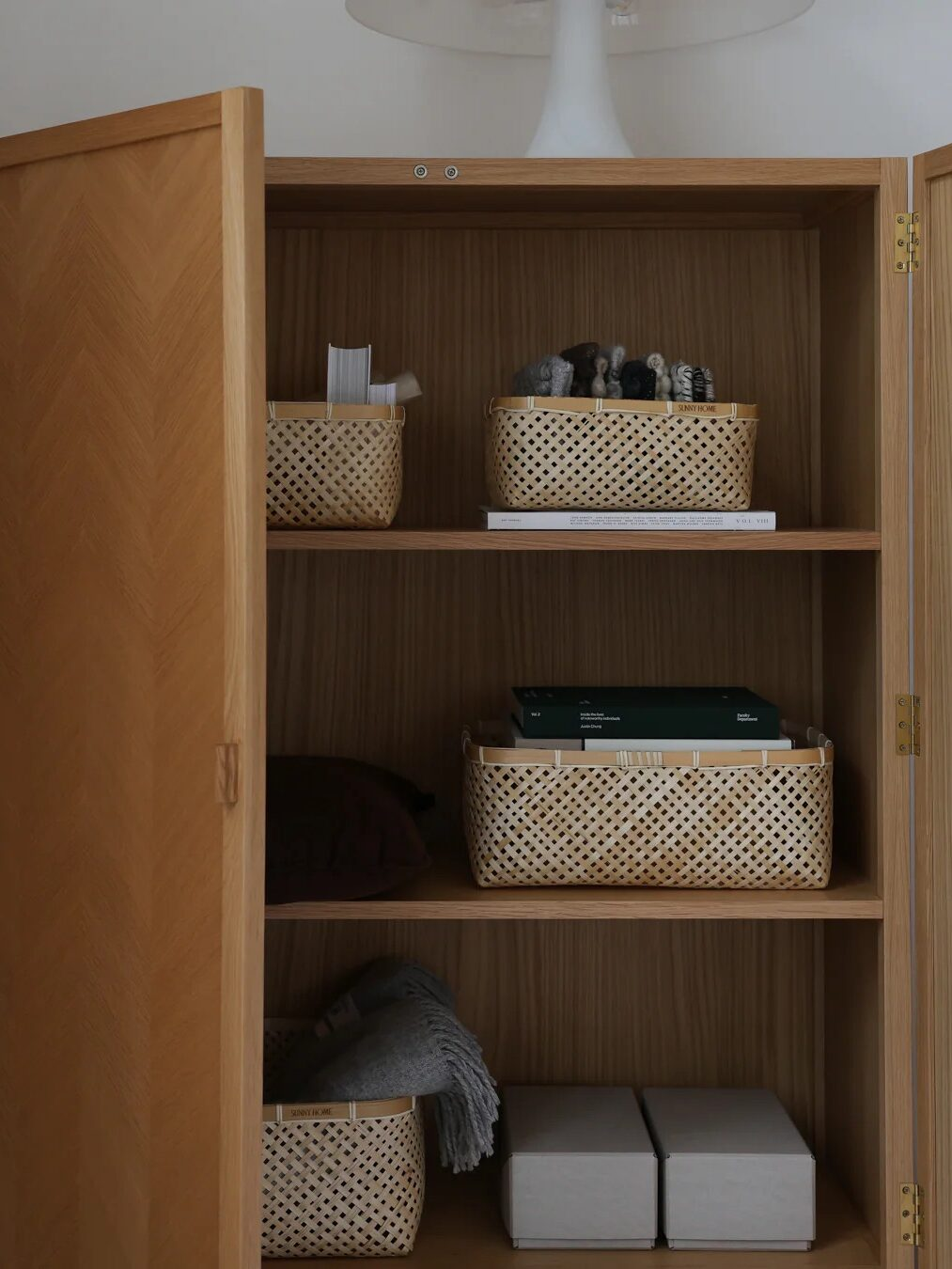 Wooden storage cabinet organized with woven baskets, folded blankets, books, and storage boxes
