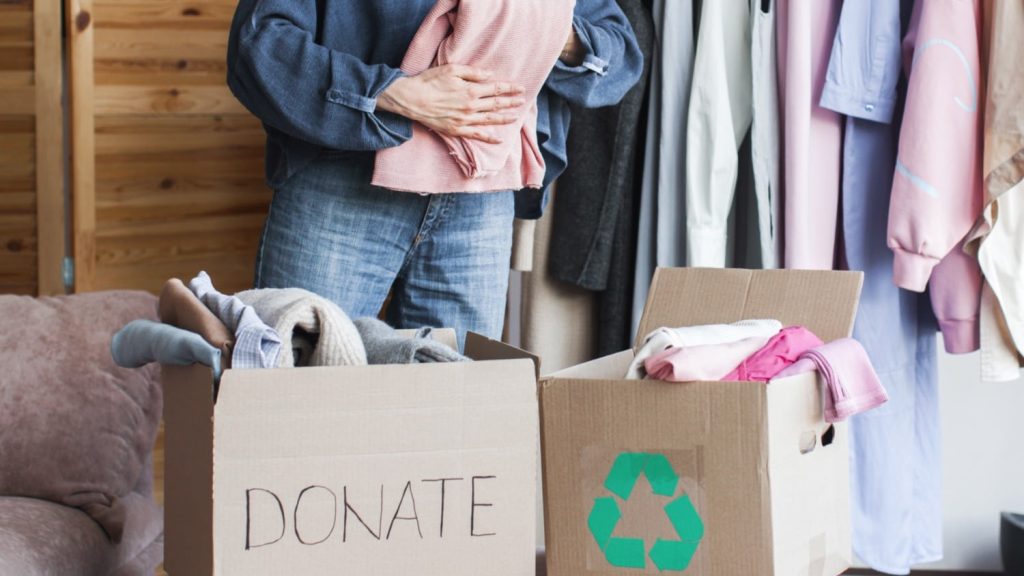 Person sorting clothes into donation and recycling boxes inside organized bedroom closet
