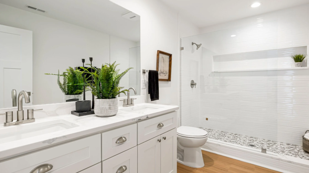 Bright white bathroom with double sink vanity, large mirror, glass shower enclosure, and indoor plants