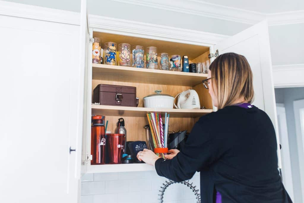 Organizing kitchen cabinet by arranging cups and household items