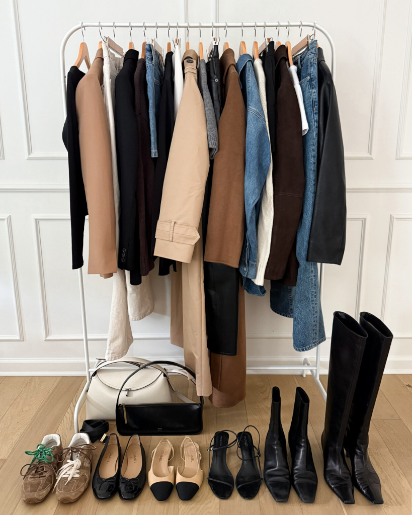 Capsule wardrobe on metal clothing rack featuring jackets, denim, handbags, and boots