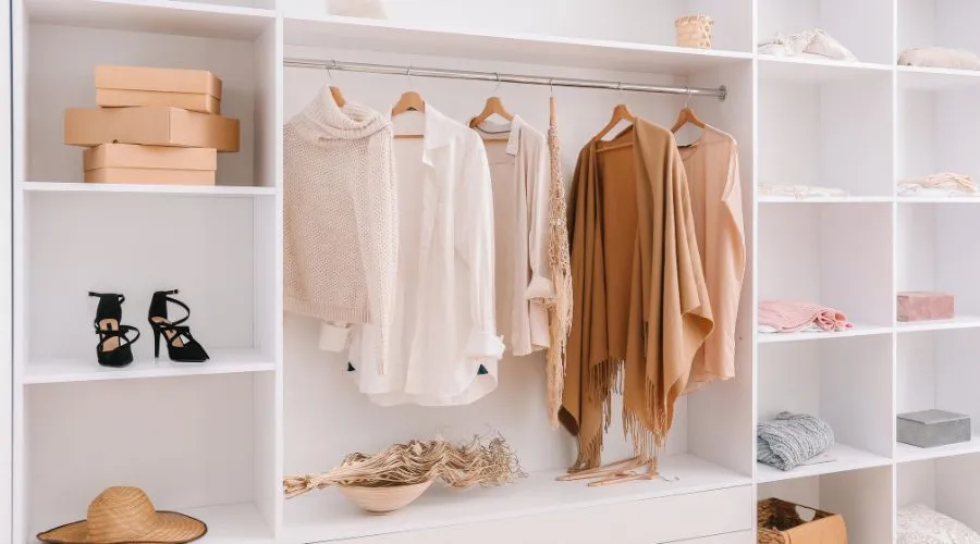 Minimalist wardrobe with neutral-tone clothing neatly hung on wooden hangers and open shelves