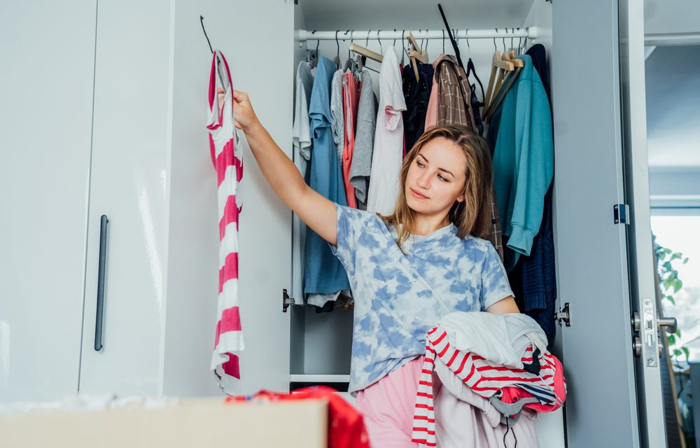 Woman sorting clothes from a wardrobe closet while organizing folded and hanging garments