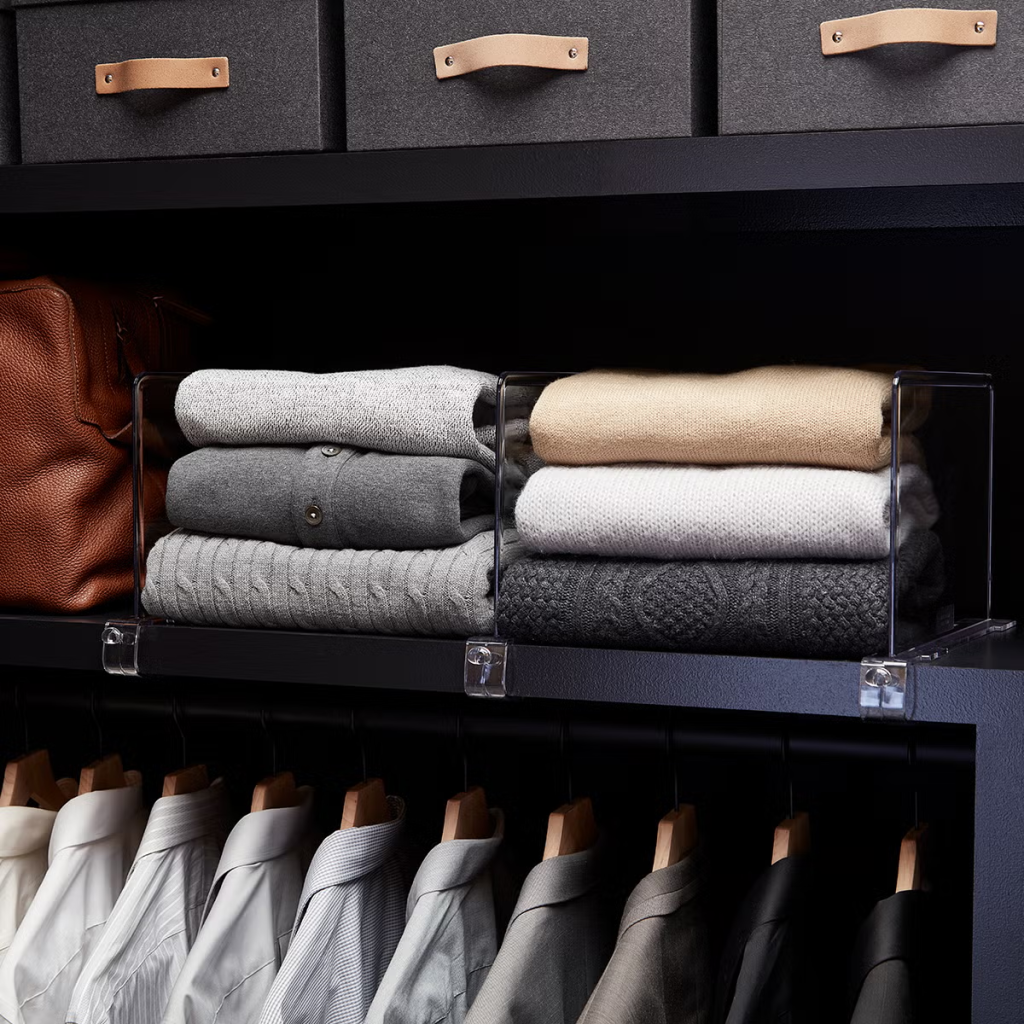 Folded sweaters organized on open closet shelves with clear dividers for neat wardrobe storage