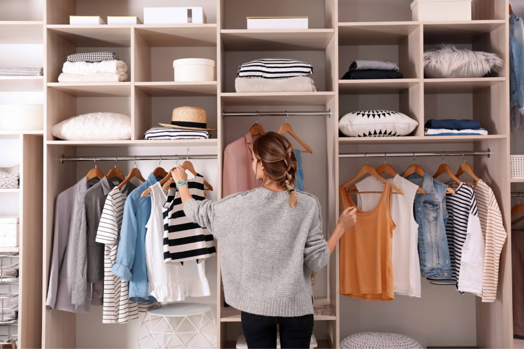 Woman organizing clothes in a spacious walk-in closet with open shelving and hanging rails