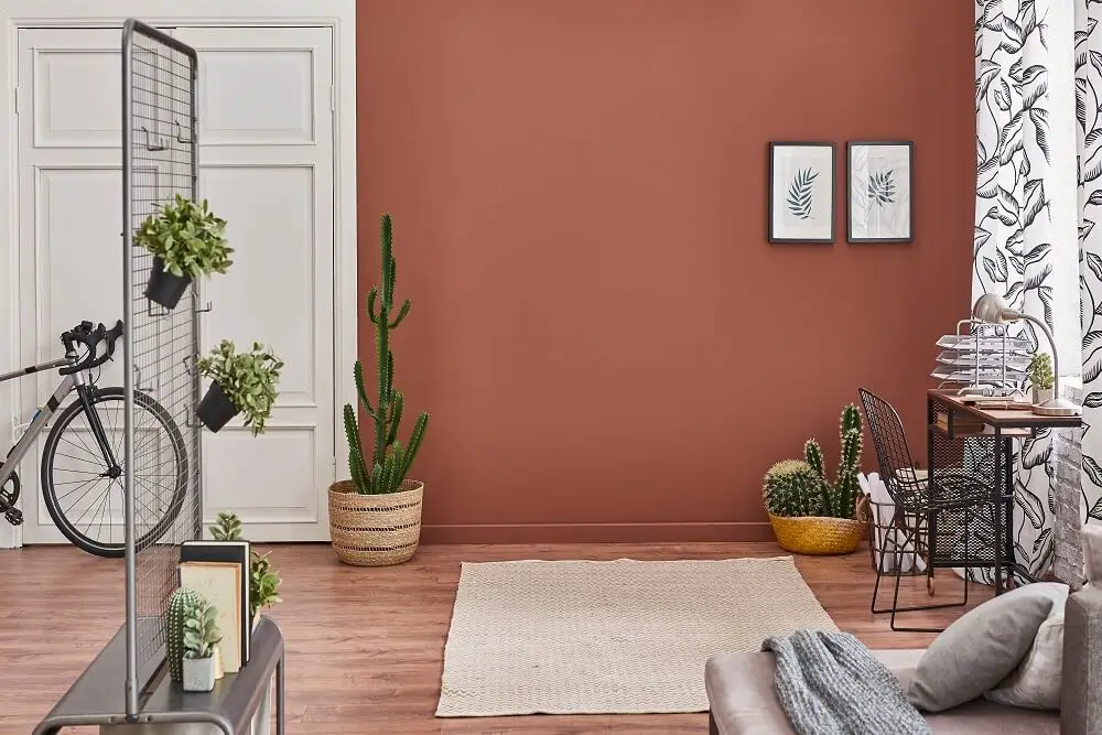 Living room with terracotta accent wall, indoor plants, modern desk, and warm minimalist decor style
