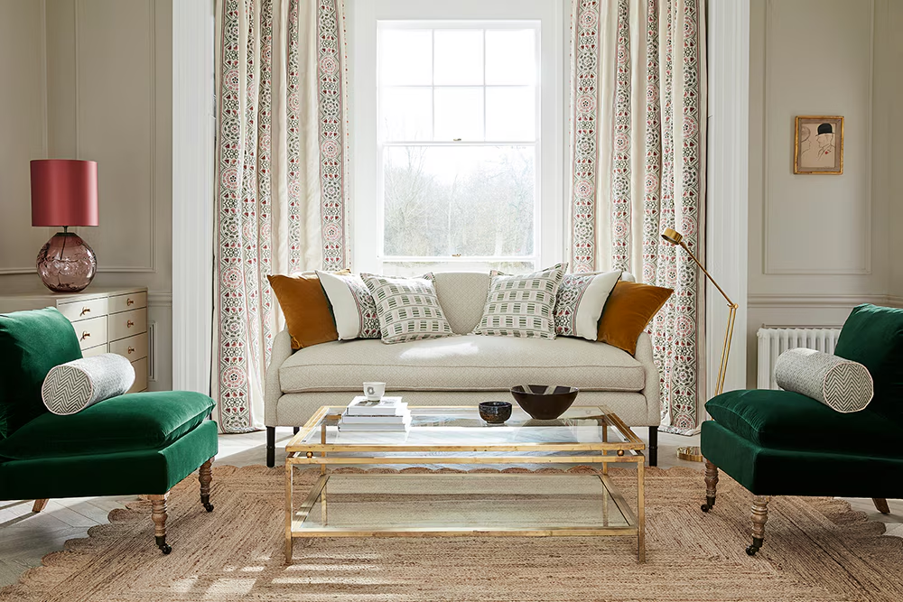 Elegant living room with green velvet armchairs, neutral sofa, patterned curtains, and jute area rug around a glass coffee table