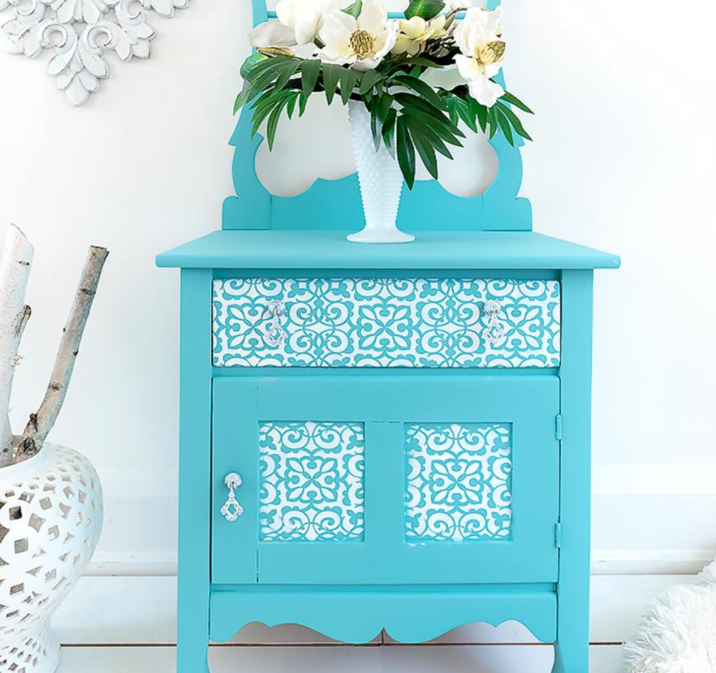 Turquoise painted accent cabinet with decorative floral pattern and white vase of flowers in a bright home interior