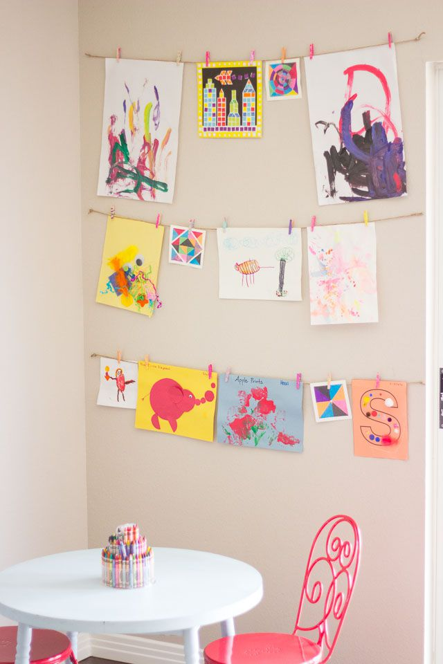 Kids art display wall with colorful drawings clipped on strings above a small table and chairs, creating a creative playroom corner