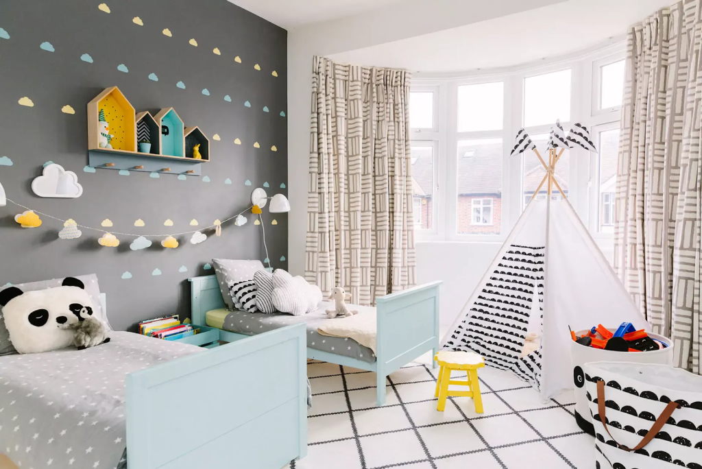 Scandinavian-style kids bedroom with twin beds, play teepee tent, toy storage basket, and cloud wall decor for a cozy play-and-sleep space