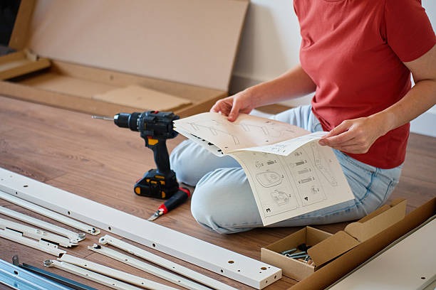 Person assembling flat-pack furniture on the floor using a cordless drill and instruction manual