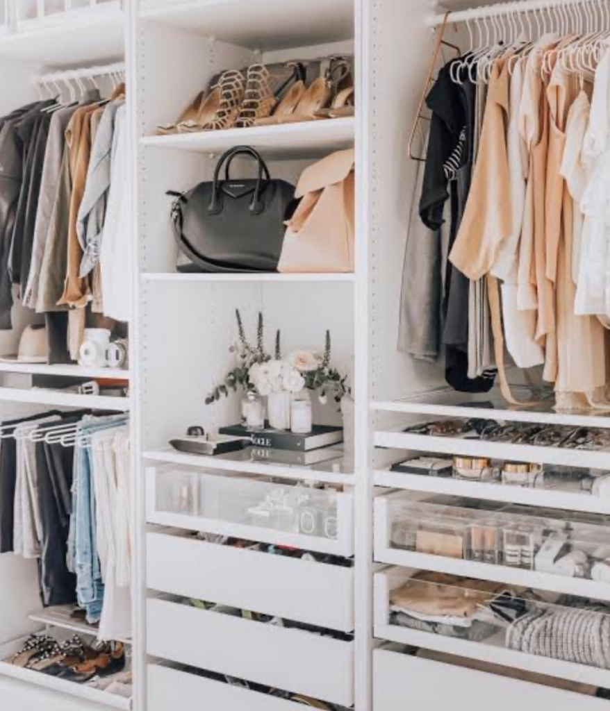 Modern walk-in closet with white shelves, drawers, handbags, and neatly arranged clothes