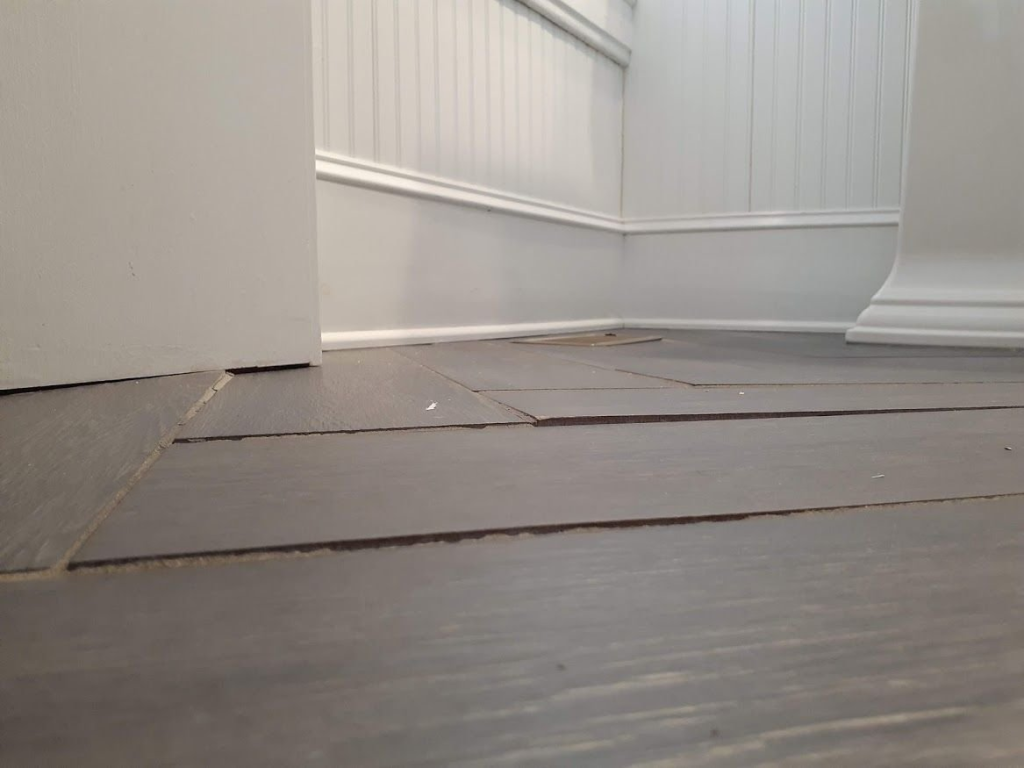 Uneven wooden floorboards showing gaps and lifting planks near wall trim in a home interior