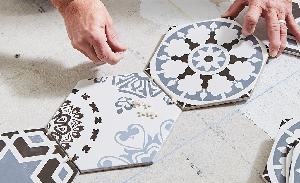 Close-up of hands installing patterned ceramic floor tiles using spacers during tile installation