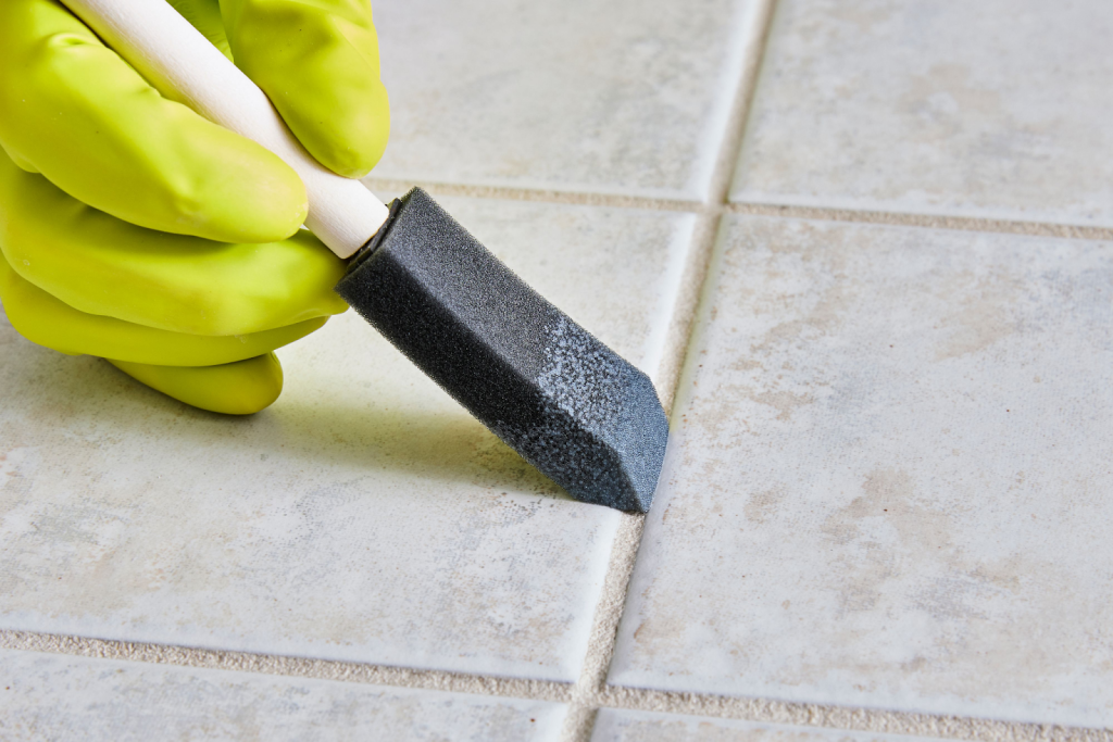 Person cleaning tile grout lines with a brush and wearing rubber gloves on a ceramic tiled floor
