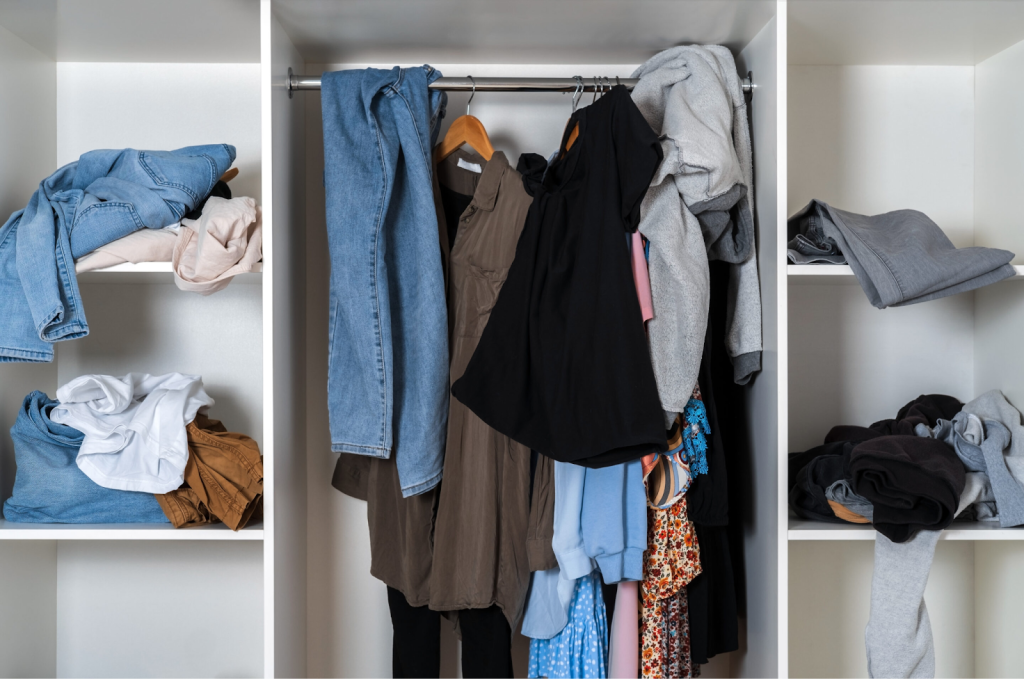 Cluttered closet with messy clothes on shelves and hanging rod before wardrobe organization